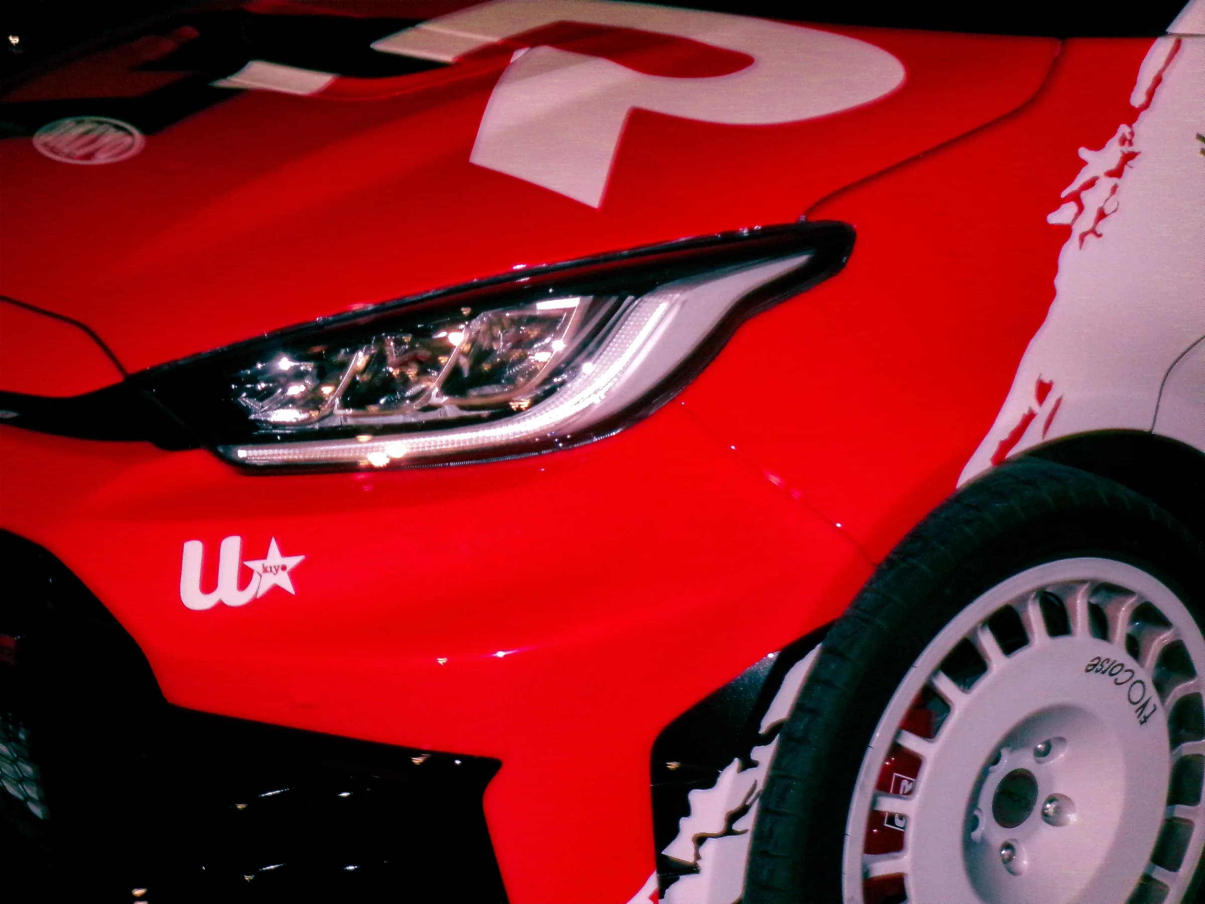 Il frontale di una Toyota GR Yaris con livrea rossa e bianca, fotografato di notte.