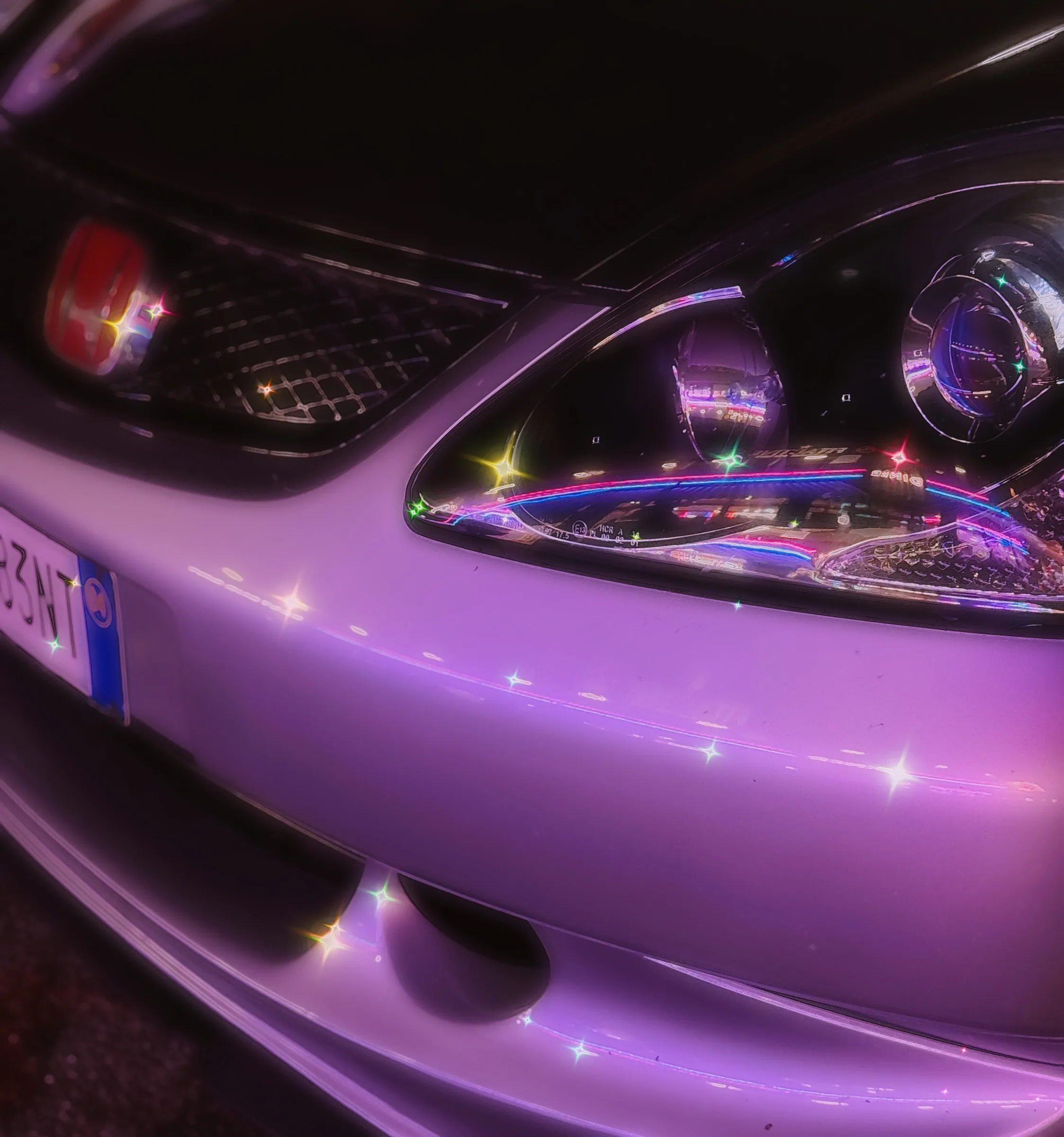 Dettaglio del faro anteriore di un'auto viola, con riflessi di luce.