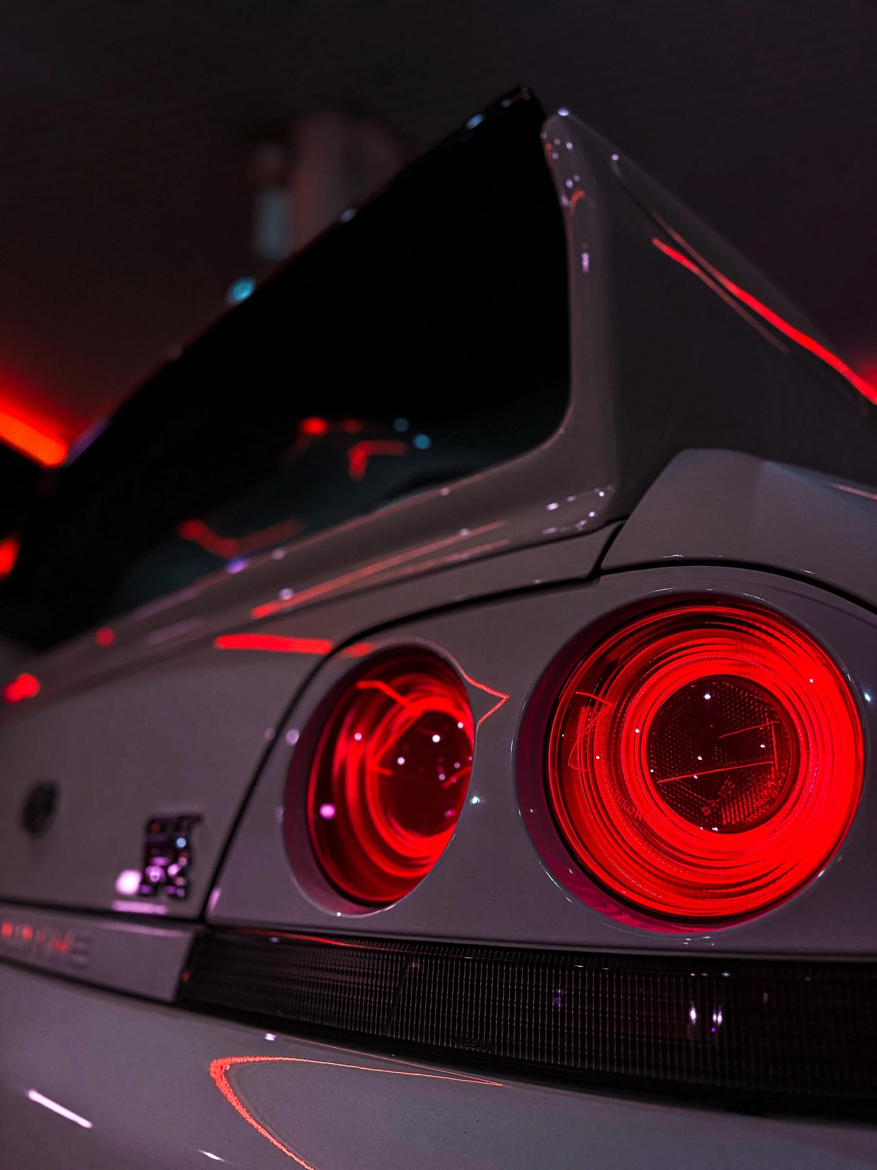 I fari posteriori circolari di una Nissan Skyline R33 illuminati di rosso nella penombra.