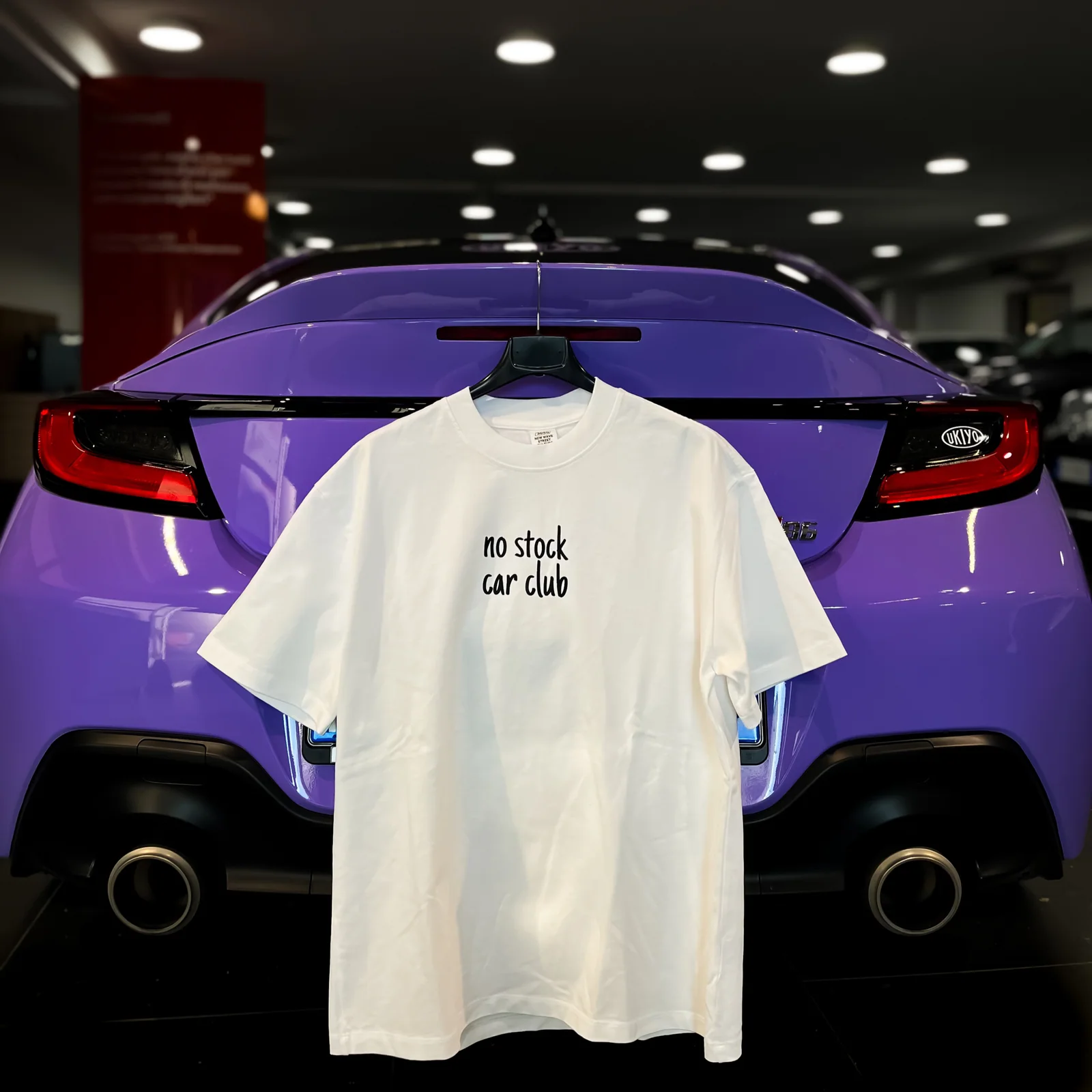 T-shirt UKIYO bianca con la scritta “no stock car club”, fotografata su una Toyota GR86 viola.